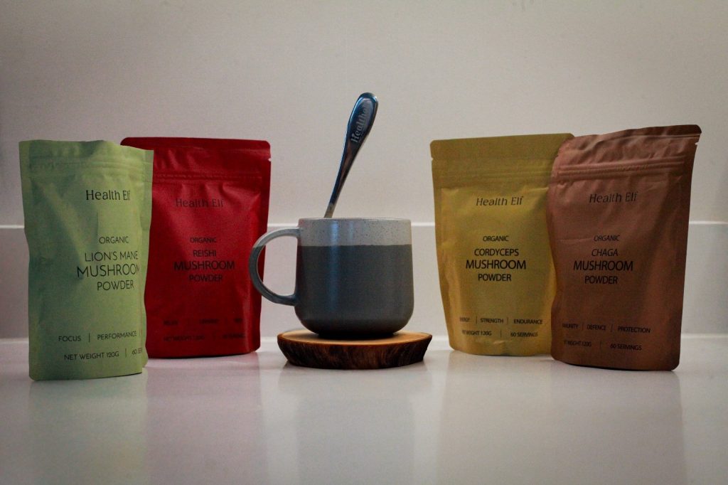 Organic mushroom powder blend including Chaga, Lion’s Mane, Reishi, and Cordyceps with a custom scoop next to a coffee mug, perfect for a balanced, natural lifestyle